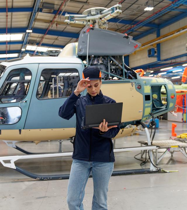 Helicopters_Marignane Woman wearing PPE stands in front of a helicopter looking at a laptop