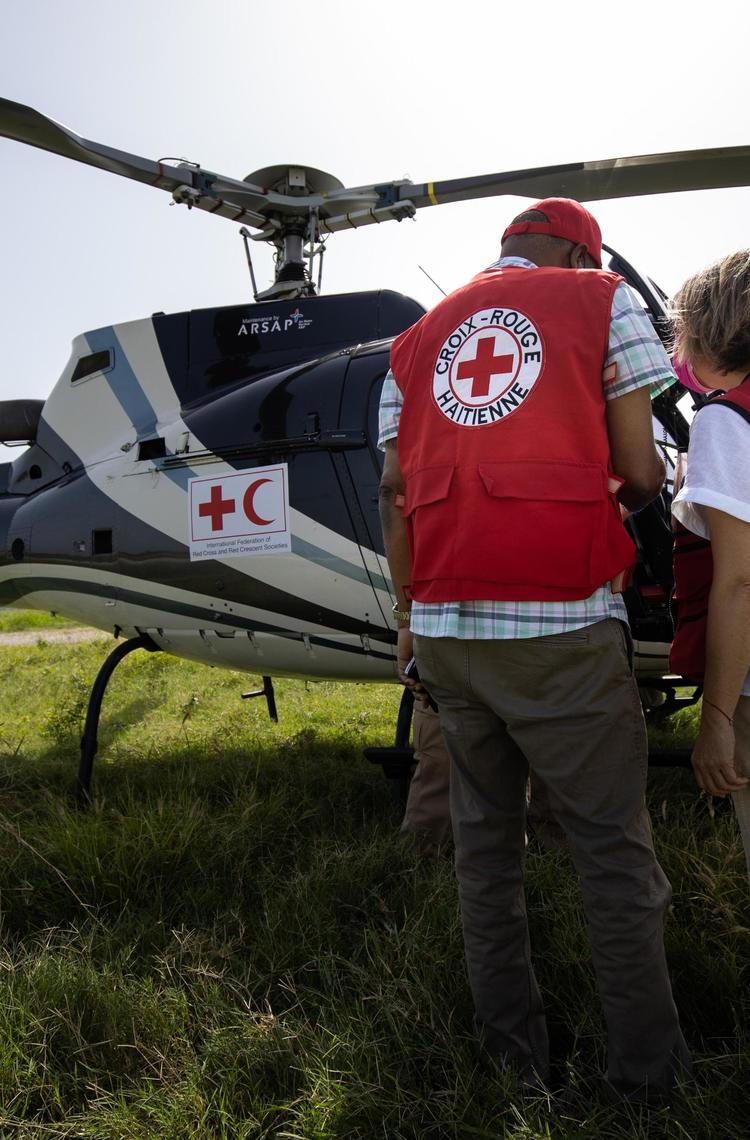 Airbus Foundation annual activity report 2023 cover image Two people standing in front of a helicopter with their back to the camera, both wear Red Cross / Red Crescent societies gear